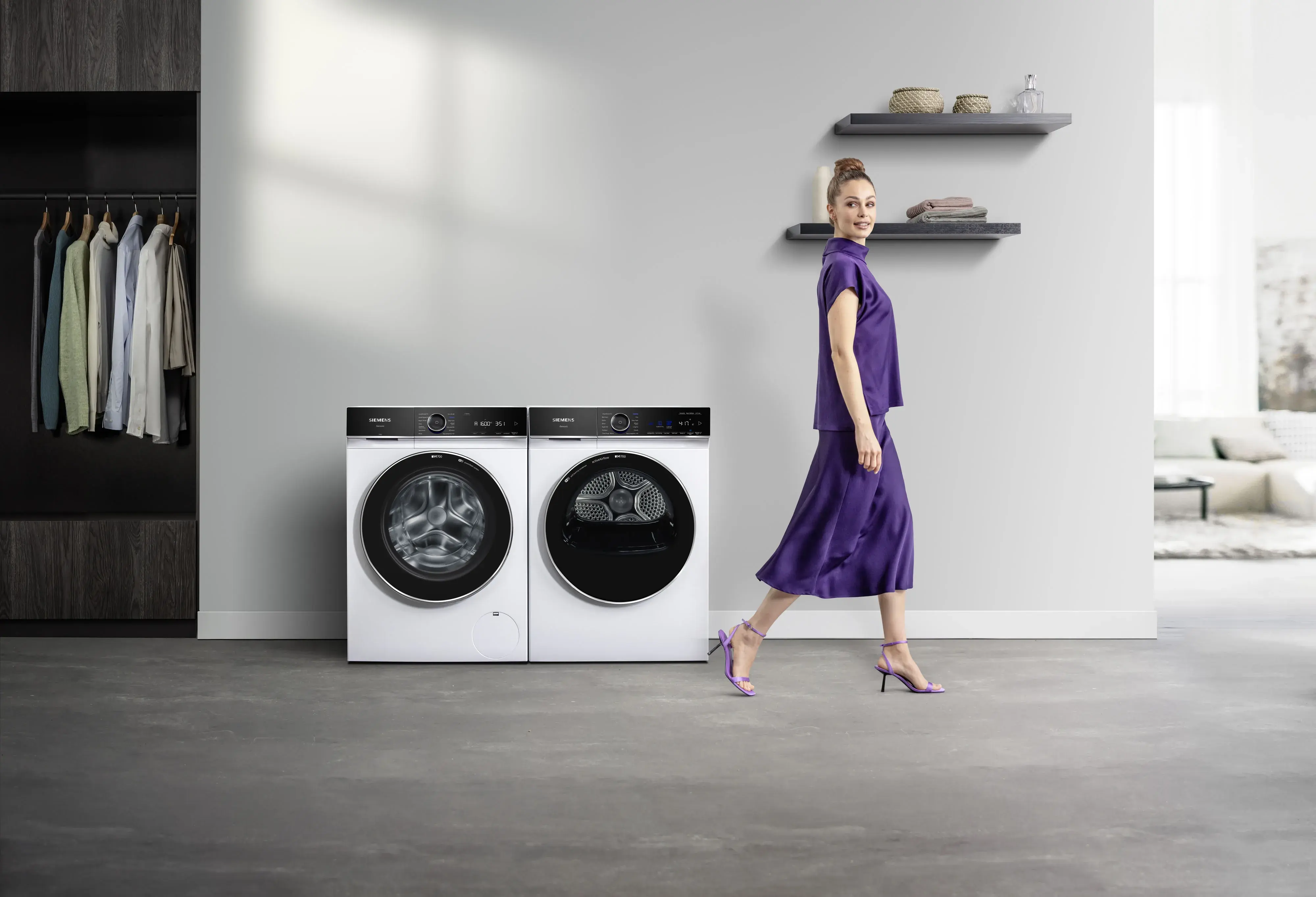 SIEMENS_iQ700 Waschmaschine und Trockner schöne Frau im lila Outfit mit hochgestecktem Haar läuft lächelnd vorbei