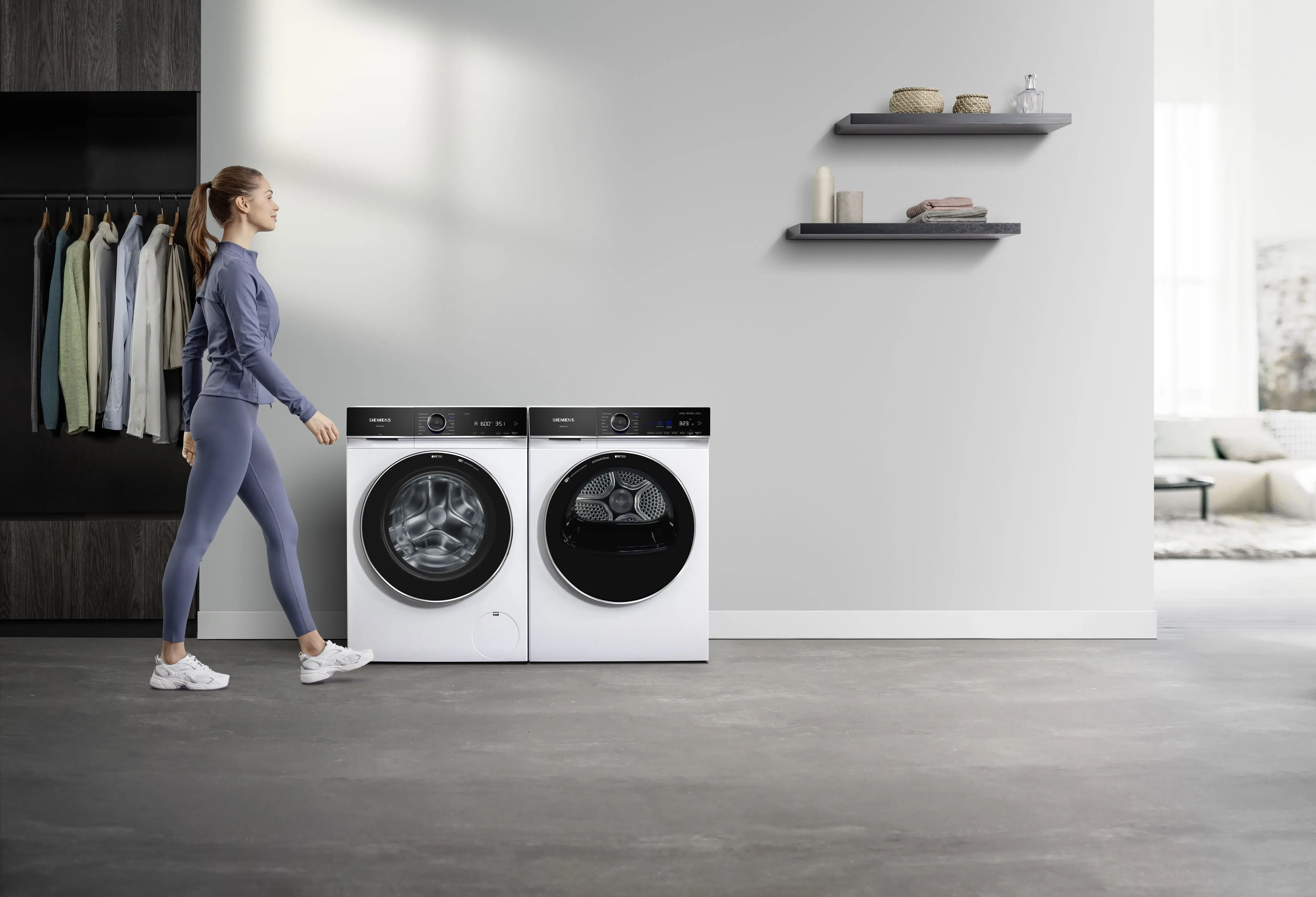SIEMENS_iQ700 Wäschetrockner und Waschmaschine varioSpeedPlus schlanke junge Frau in lila Sportkleidung läuft vor Waschmaschine und Trockner